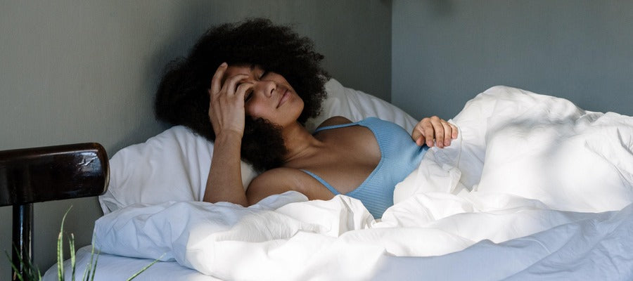 woman with Afro hairstyle waking up in bed with dry eyes in sunlit room