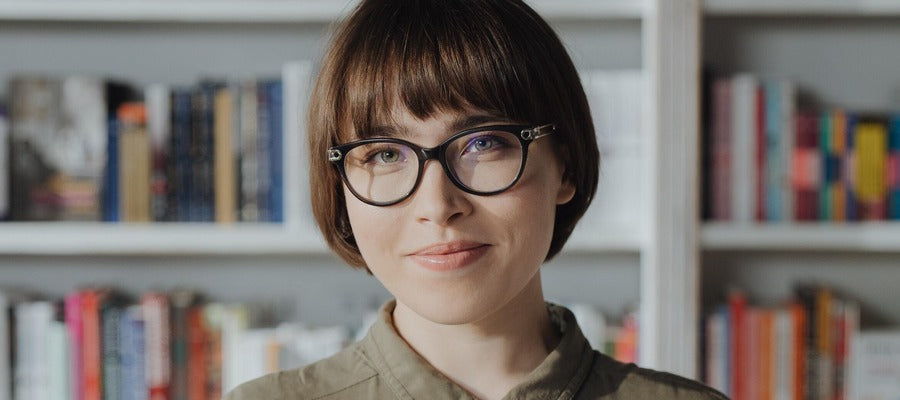 woman with glasses smiling gently with blurred bookshelves in the background