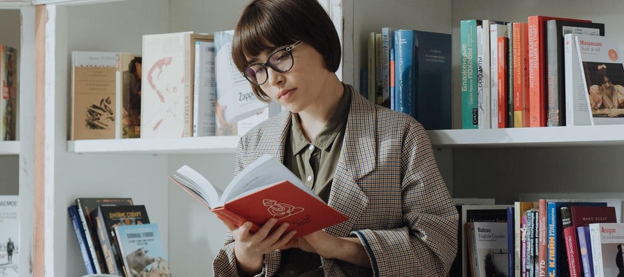 woman with glasses reading a book with red covers