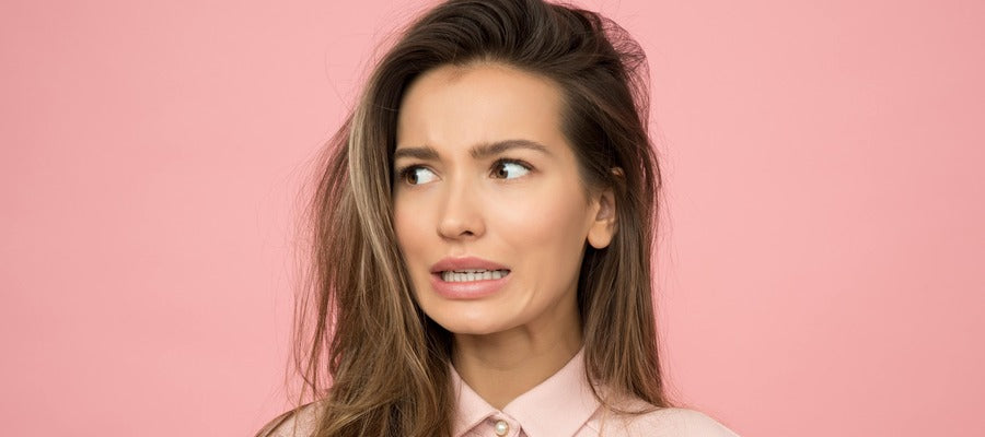 woman with long hair looking sideways with worried expression against pale pink background