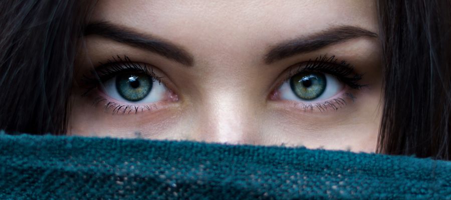 closeup of woman with beautiful eyes hiding her face behind a blue cloth