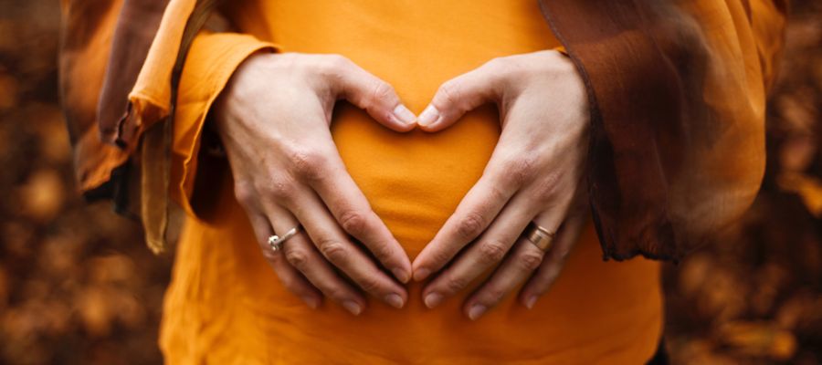 woman in orange shirt holding hands in the shape of heart over stomach