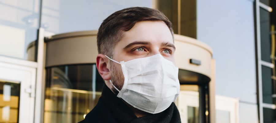 man with blue eyes wearing white disposable face mask in front of hotel entrance