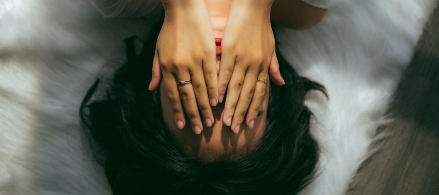 woman covering eyes with hands lying on bed
