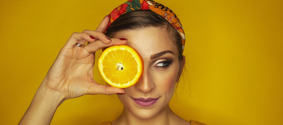 portrait of woman holding an orange slice over her right eye