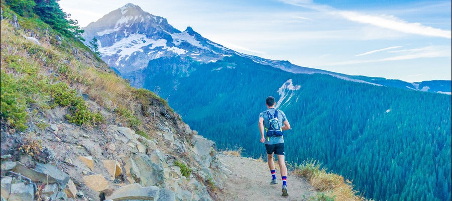 man running on hiking trail with snow-capped blue mountain peak in the background