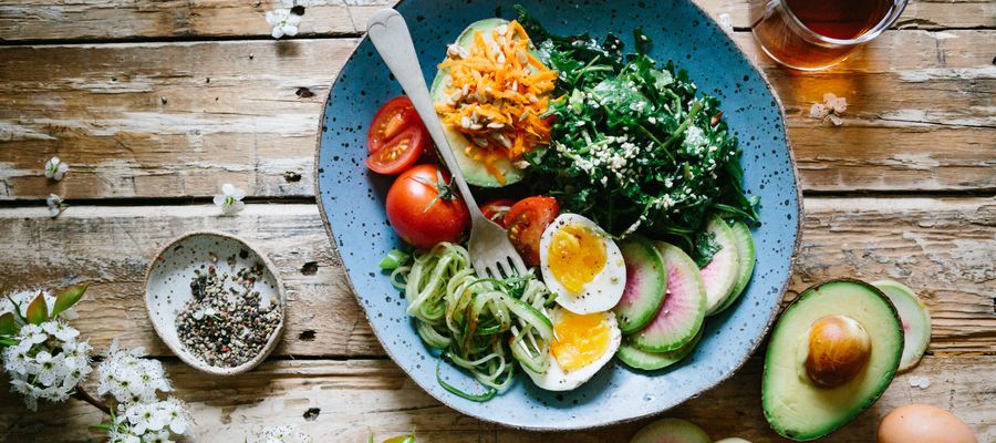 blue plate with eggs leafy greens carrots avocado seeds tomatoes and other food on wooden table