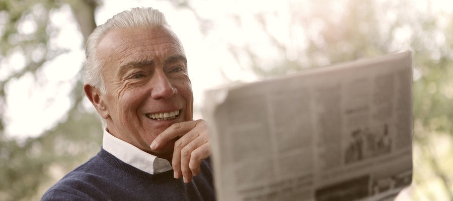 smiling old man reading newspaper he holds in front of himself