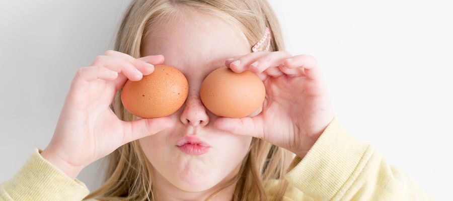young blond and pale girl in yellow sweater holding two eggs over her eyes