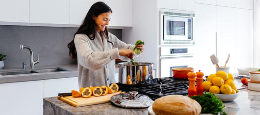 woman with dark hair cooking healthy meal at home in modern kitchen with lemons, bread, and other foods on the island counter