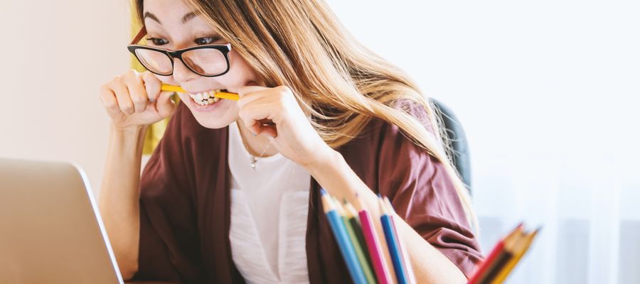 young woman with eye grasses biting pencil before a screen because she is stressed