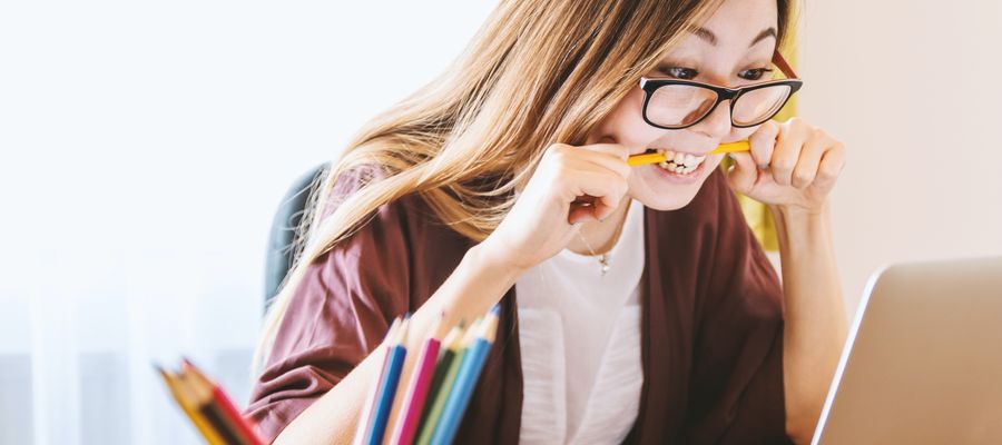 young stressed woman with eyeglasses biting pencil in front of the computer
