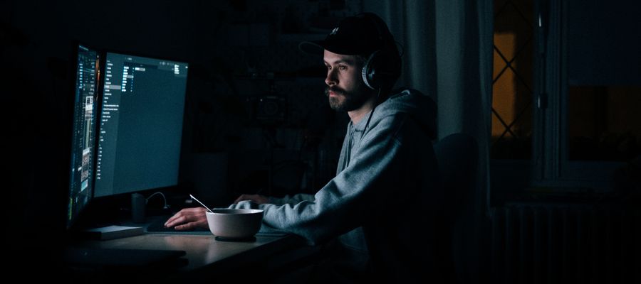 man with a cap and food bowl looking at screens at night in a dark room