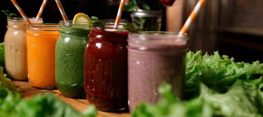 smoothies of different colors lined on table in glass jars