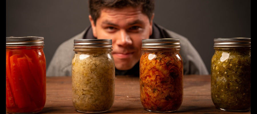 man looking through glass jars with probiotic foods at viewer