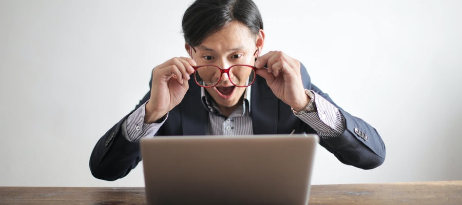 man in business suit holding red eyeglasses before computer amazed at eye facts