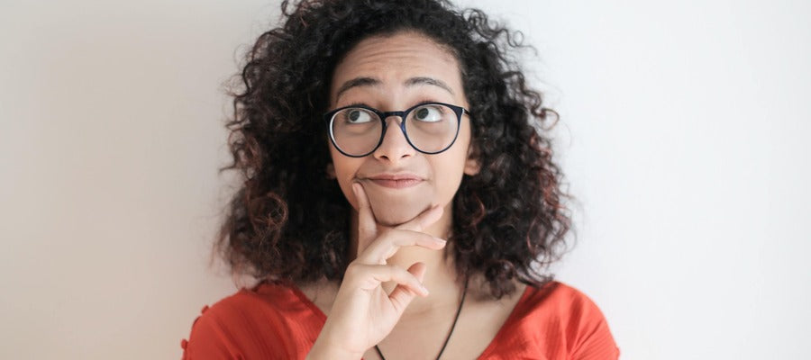 woman with glasses and curly hair thinking with eyes up and hand to her chin