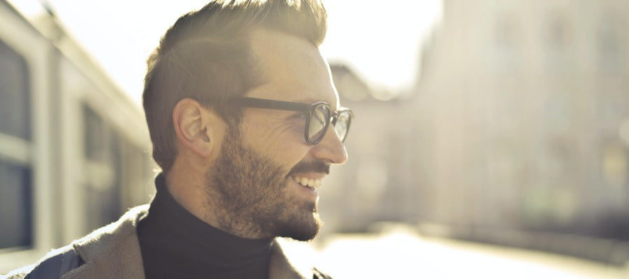 man with glasses smiling with head turned to one side against blurry sunlit background
