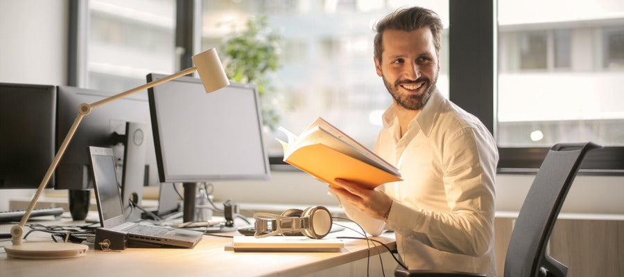 man in white shirt smiling at office desk while holding a notebook