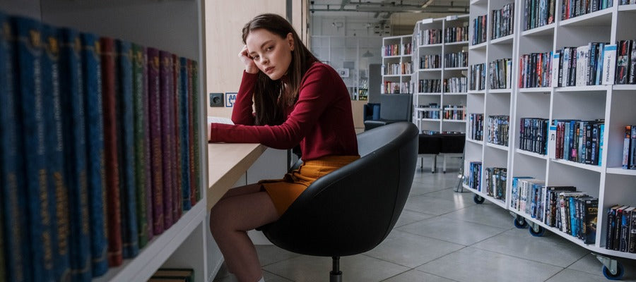 teenage girl sitting on a chair and looking at viewer in a modern library with bookshelves in the background
