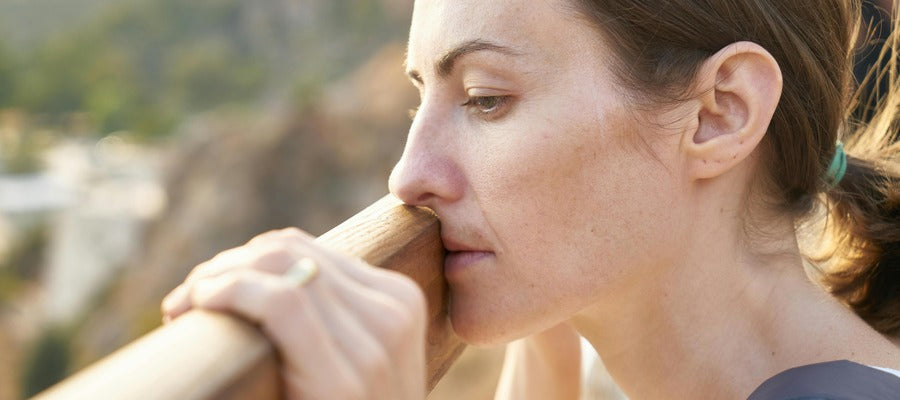 woman resting mouth and nose on wooden railing looking down and feeling depressed