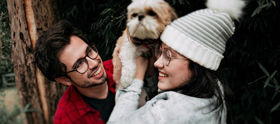 man and woman with glasses holding fluffy dog between them and smiling