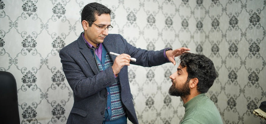 man sitting down being examined by eye doctor in a room with patterned wallpaper