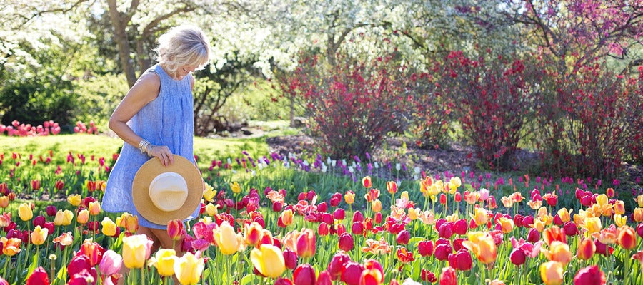 woman in blue dress with hand in hand walking through springtime scenery with blooming tulips and greenery and pollen