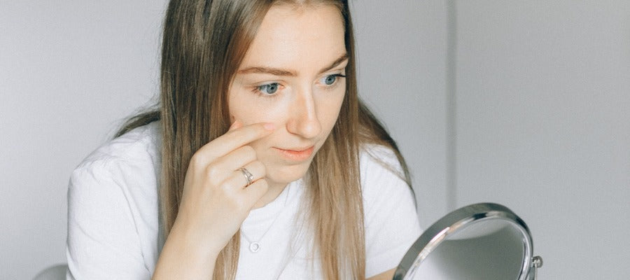 woman with blue eyes in white shirt looking into round mirror after putting on contact lenses