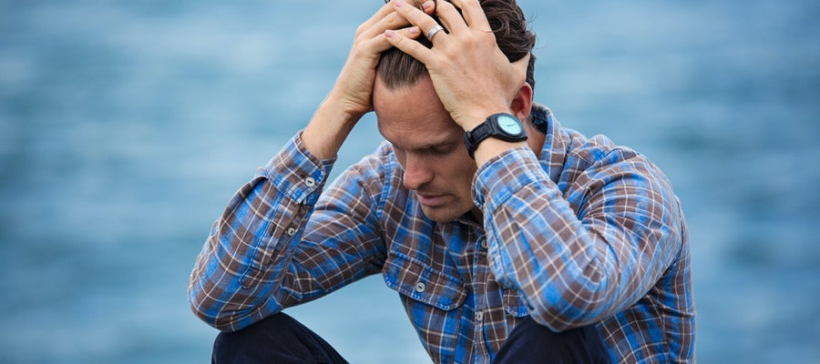 anxious man in checkered shirt holding his head in his hands by the sea