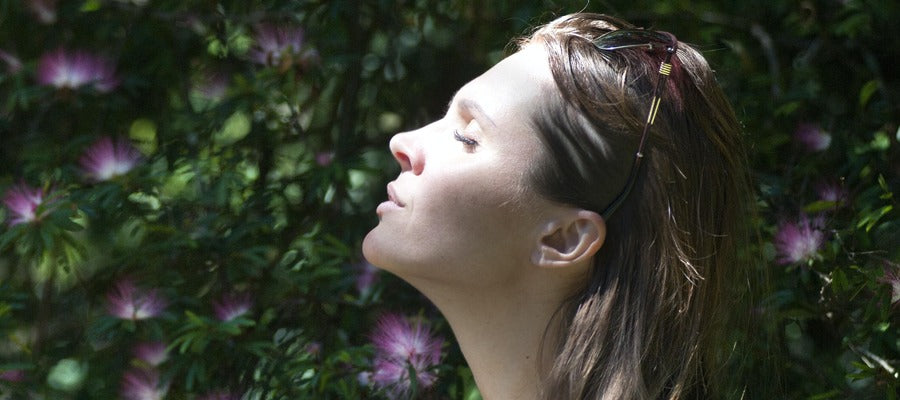 woman with closed eyes holding face up in the sun against blurry green nature background