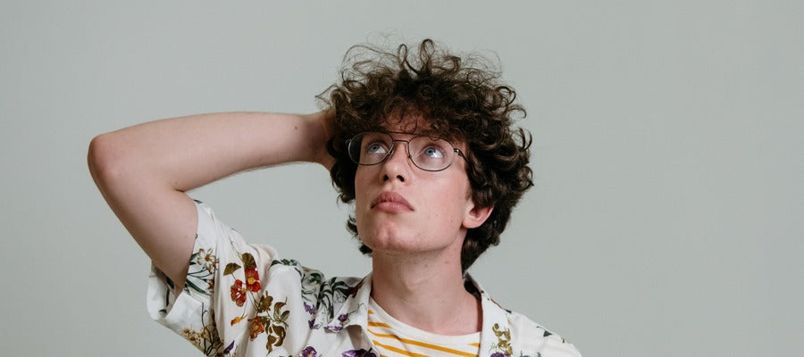 young man with glasses and big curly hair looking up with one hand behind his head