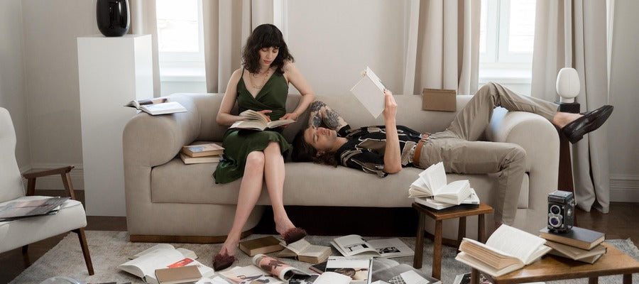 woman siting and man lying on couch reading in the living room with books littering the floor