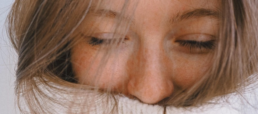 closeup of woman with closed eyes hiding her mouth in white turtleneck 