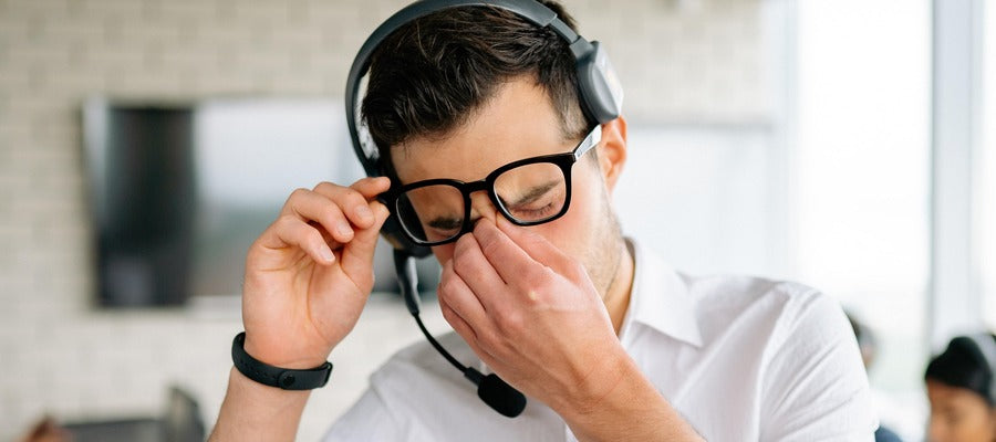 man with eyeglasses and microphone headphones rubbing eyes suffering from computer vision syndrome