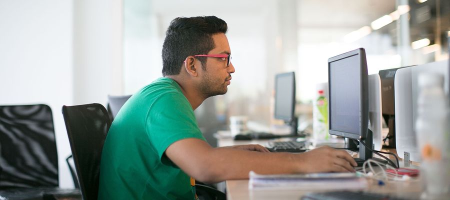 man with glasses in green shirt slouching before computer desk at work