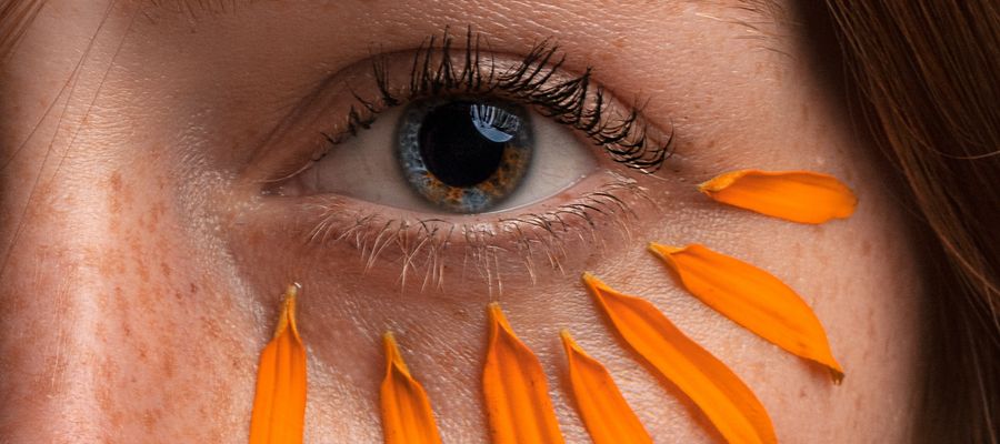 closeup of woman's eye with orange petals below it