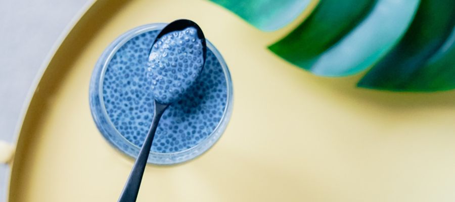 blueberries chia seed pudding in a jar with spoon on yellow background
