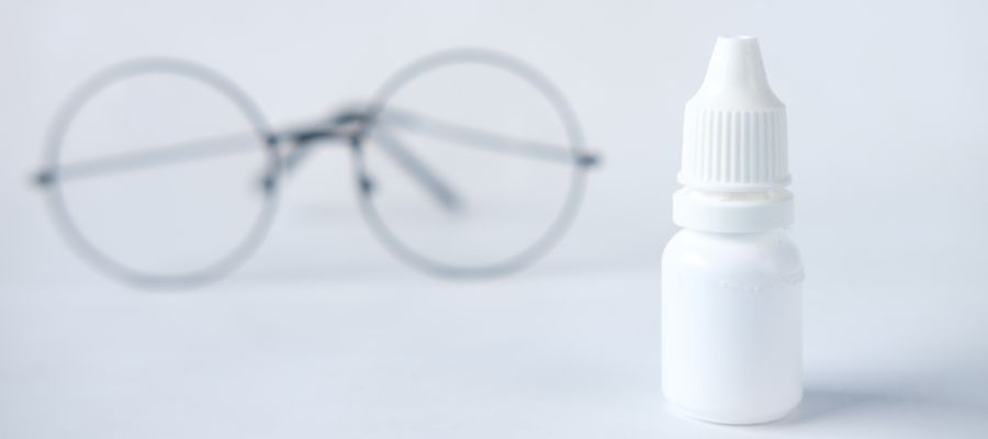 closeup of eye drops bottle with pair of round glasses in the background