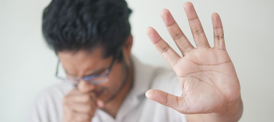 man with eyeglasses sneezing while holding palm with fingers extended in front of the viewer