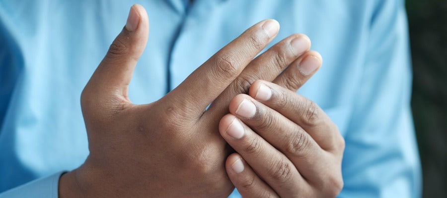 man in light blue shirt holding finger joints affected by arthritis with one hand