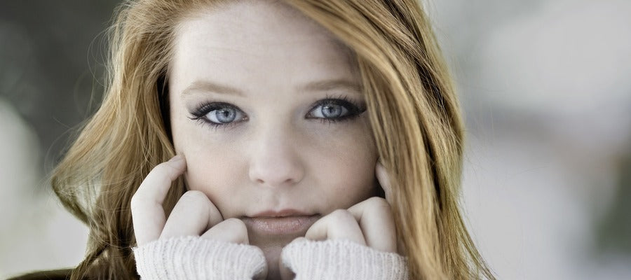 young woman with blue eyes and long woolen sleeves touching her face with her hands