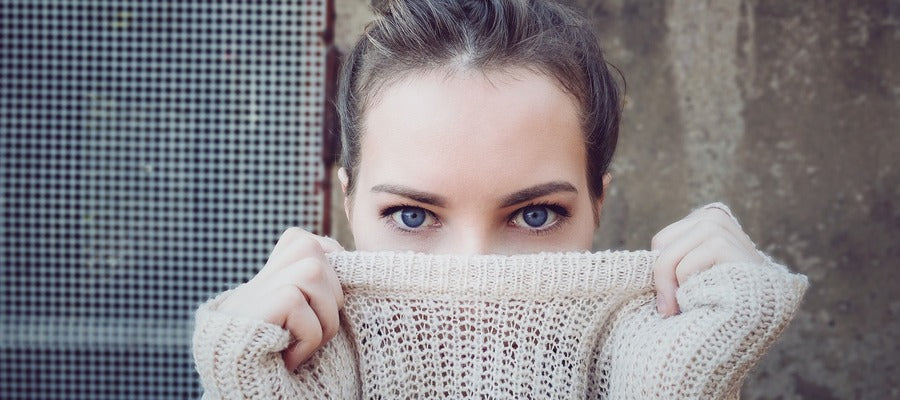 woman holding knitwear collar with both hands over her face below blue eyes